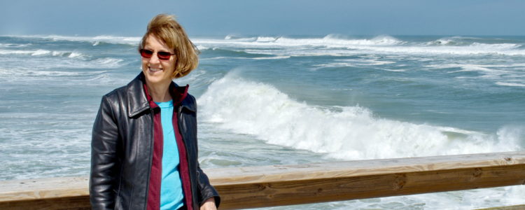 Woman in leather jacket standing by the ocean on a windy day.