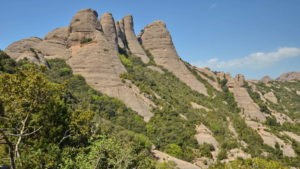 Rocky mountain peaks with greenery under a clear blue sky.