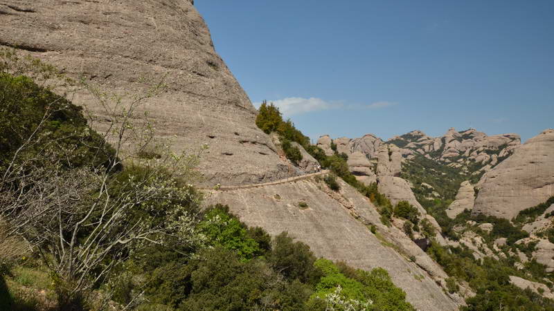 Hikers walking along a narrow mountain trail on a rocky slope.