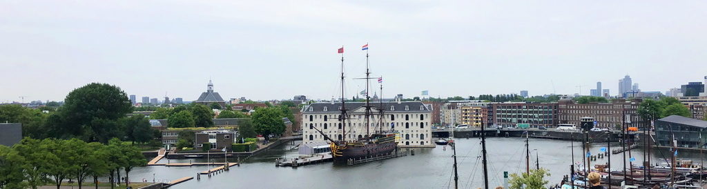 Historic tall ship docked near waterfront buildings under a cloudy sky.