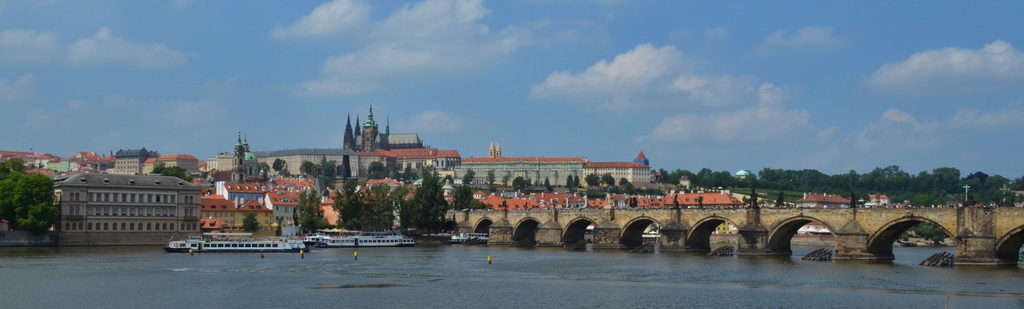 Historic castle and stone bridge over a river under a blue sky.