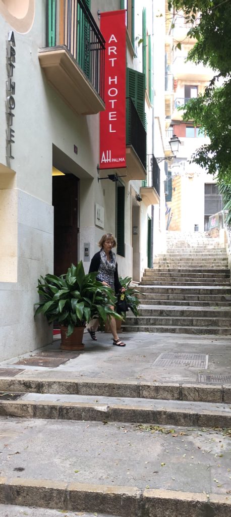 Woman walking down a narrow street with potted plants and stairs.