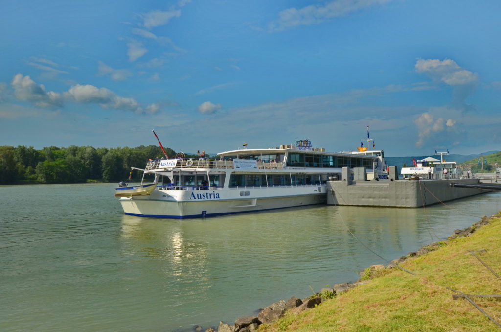 A passenger boat named 'Adriatic' cruising on a calm river under a blue sky.