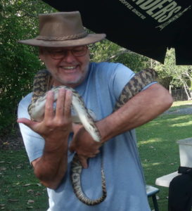 Man smiling while holding a small alligator outdoors.