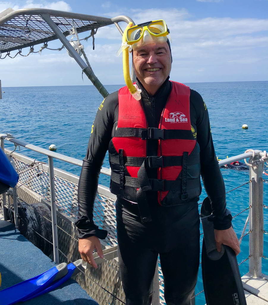 Man in wetsuit and red life jacket on a boat by the sea.