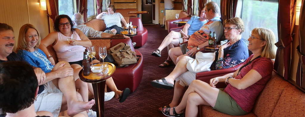 Passengers relaxing in a train's lounge car with drinks and casual seating.
