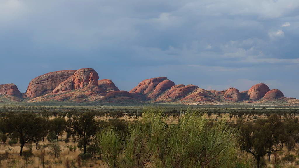 Red rocky formations under a cloudy sky in a desert landscape.