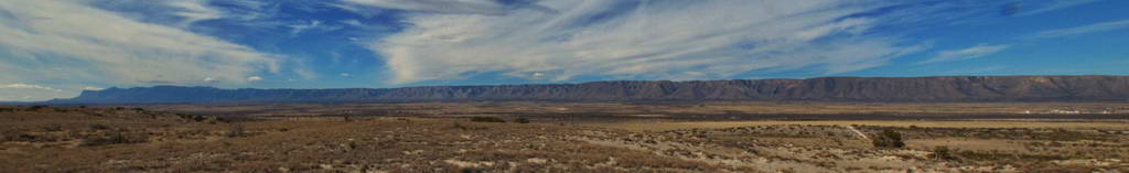 A vast desert landscape under a partly cloudy sky with distant mountains.