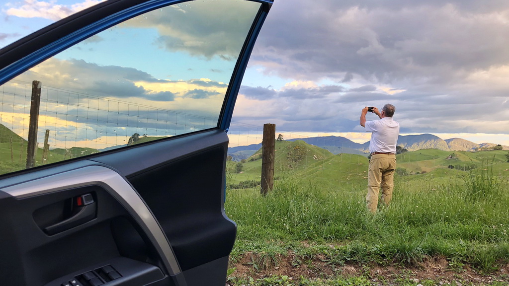 Person looking through binoculars near a car with scenic mountain view.