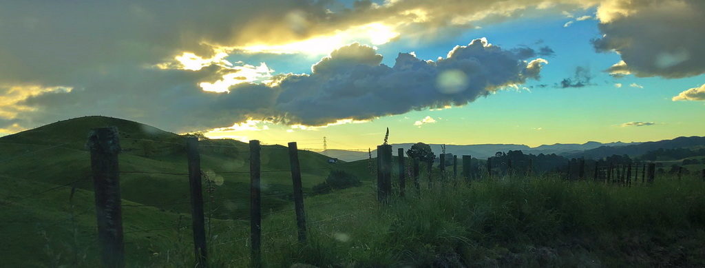 Sunset sky over a rural fence and grassy field.