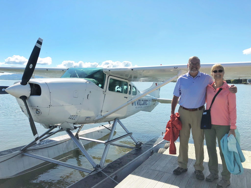 A man and woman stand beside a small seaplane on a dock.