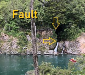 A rocky fault line beside a calm water body with a tree in the foreground.
