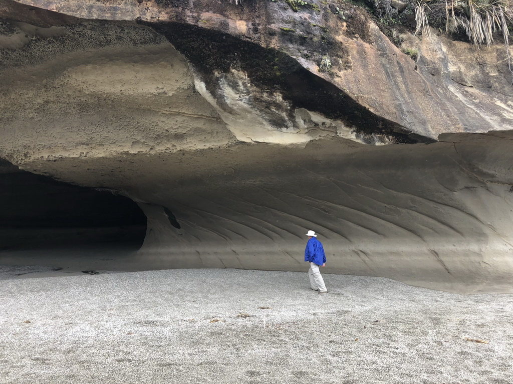 Person walking near a large rock cave entrance.