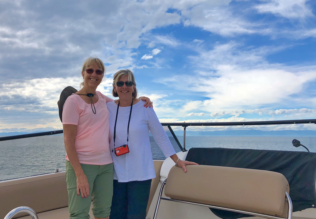 Two women standing on a boat with a cloudy sky background.