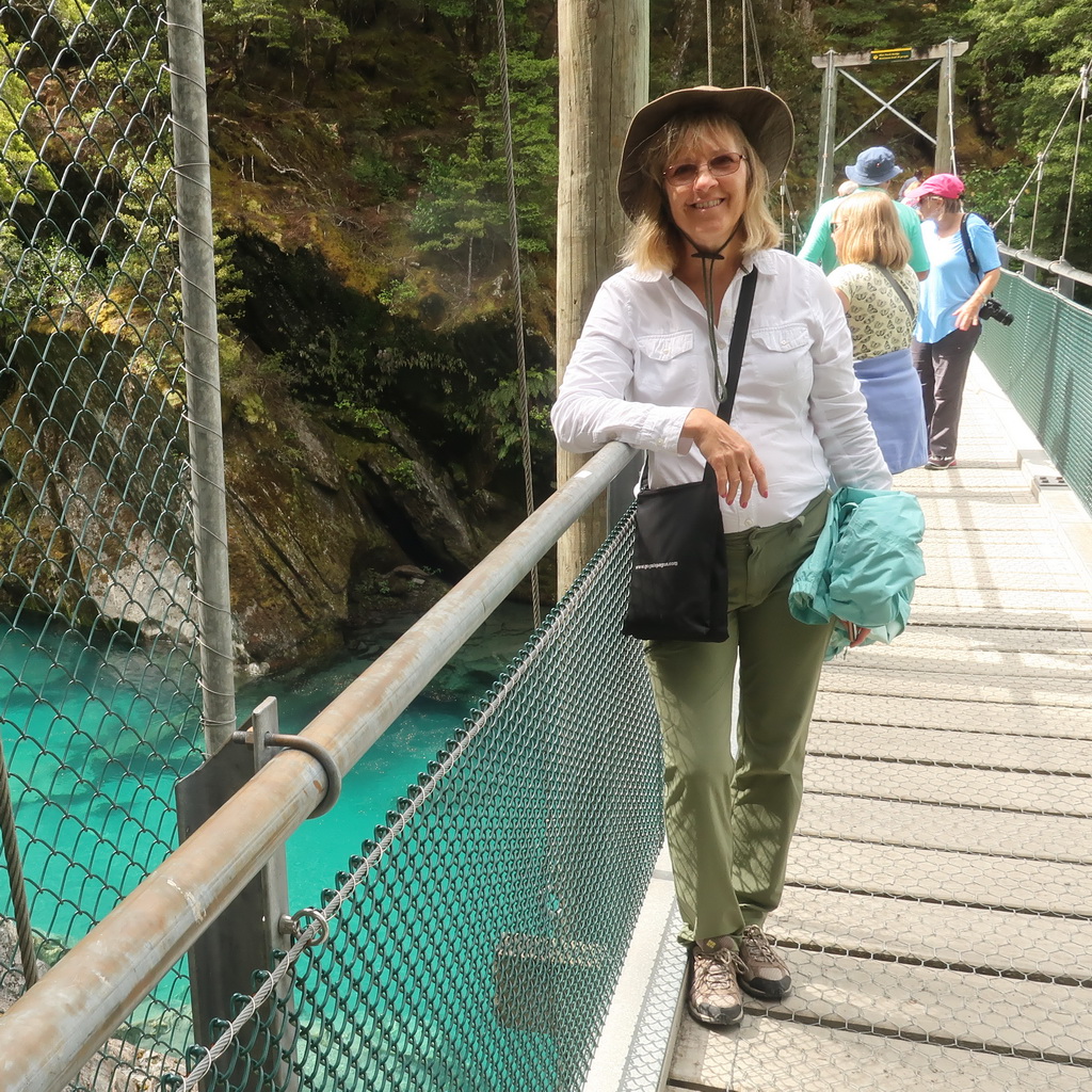 A woman smiling on a suspension bridge over turquoise water.