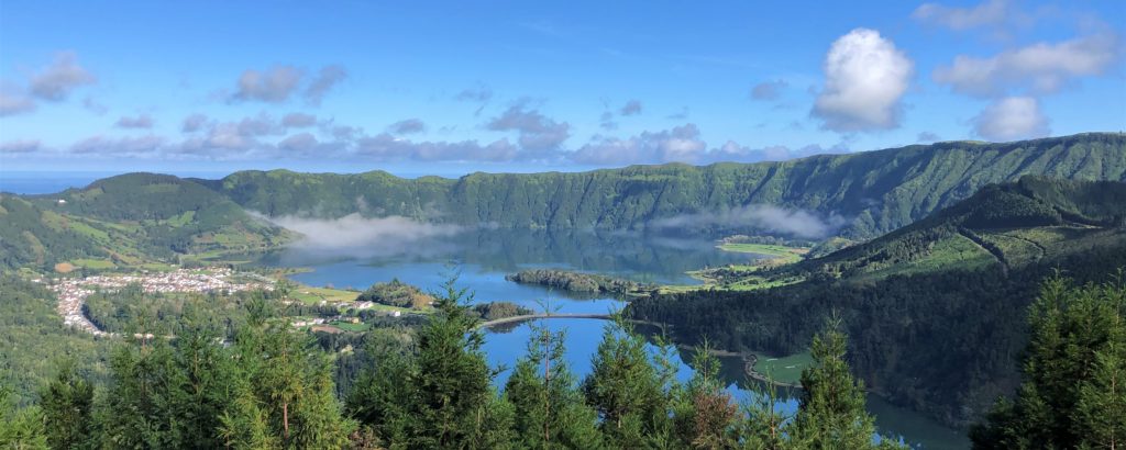 Scenic lake surrounded by lush green hills under a blue sky.