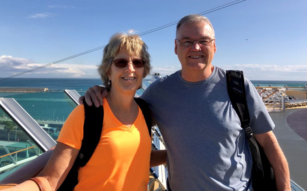 A smiling couple posing outdoors on a sunny day near the water.