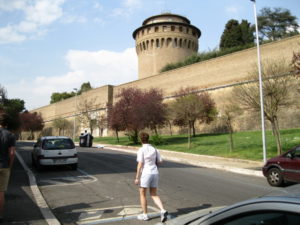 A person walking near a historic stone fortress with a large round tower.