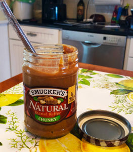 Open jar of Smucker's Natural Strawberry Jam with spoon inside on kitchen table.