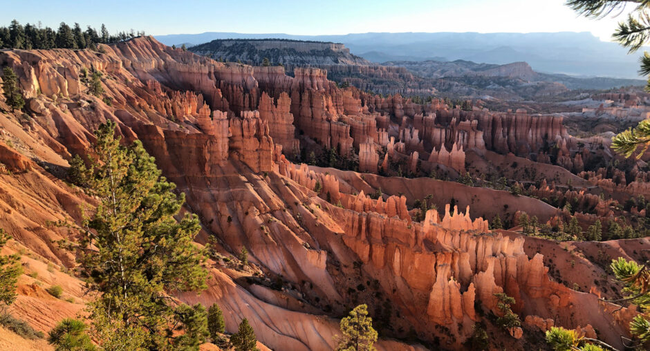Sunlit hoodoos and rugged cliffs in a vast desert canyon.