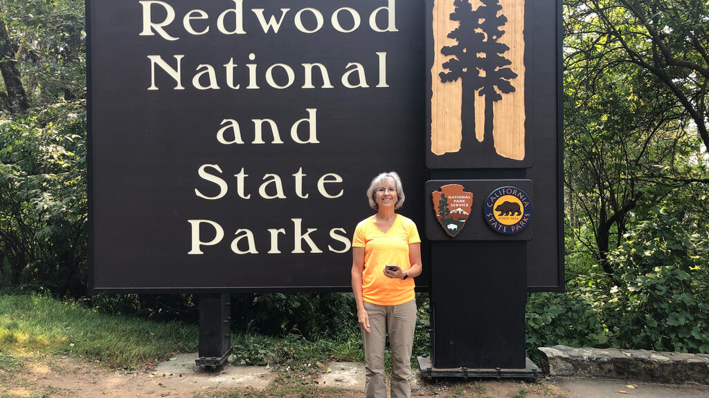 Person standing in front of Redwood National and State Parks sign.