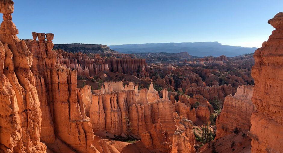 Sunlit rock formations in a vast desert canyon under a clear blue sky.