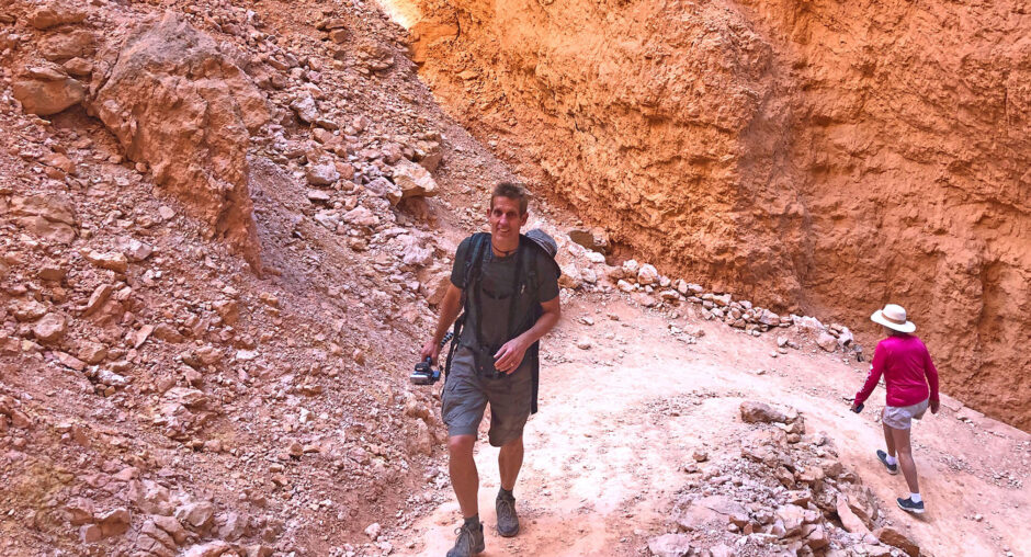 Man hiking through a rocky canyon holding a camera.