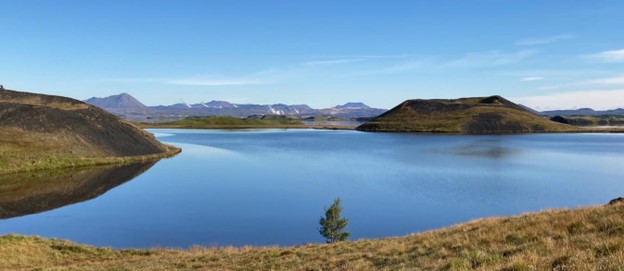 Calm lake with distant mountains under a clear blue sky.