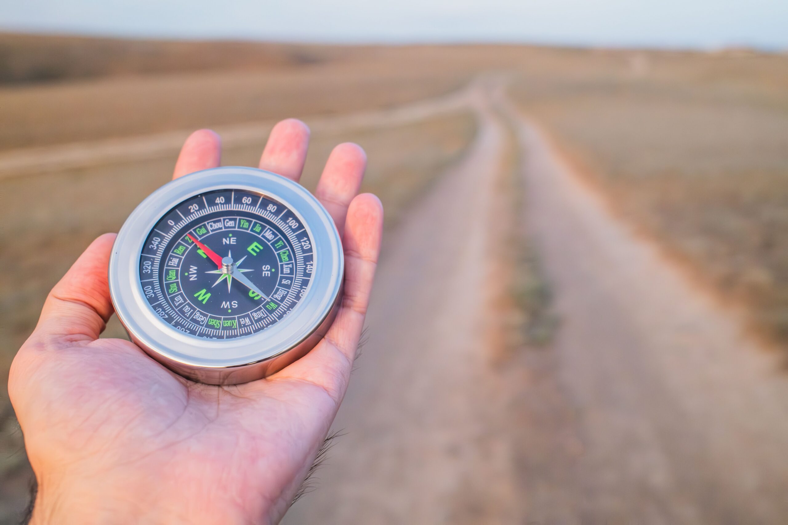Hand holding a compass pointing down an open path, symbolizing goal setting